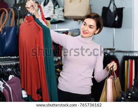 Young happy  female shopper examining turtleneck sweaters in women`s cloths shop