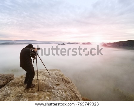 Photographer framing picture with eye on viewfinder. Photo enthusiast  enjoy work of fall nature on rocky summit. Dreamy landscape, misty sunrise in a beautiful valley below