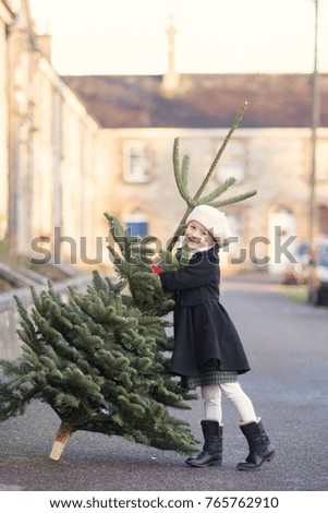 
Little girl in a old fashioned coat with a Christmas tree on vintage irish street