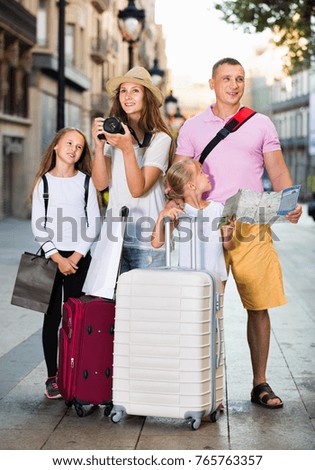 Cheerful positive smiling tourist family using map and taking photo of city while strolling with camera and phone 