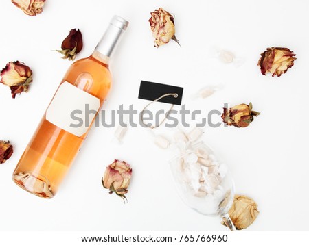 Flat lay. Minimal style. Minimalist trend photography. A bottle of rose with a composition of dried roses. Wine bottle, glass and on white table. Top view