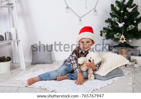 Beautiful 3 year old boy in Santa Claus hat posing in studio with New Year decor