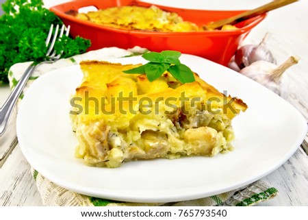 Casserole from mashed potatoes with fish fillets in a plate on a napkin on a light wooden board background