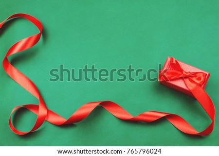 Red gift box with a ribbon on green background. Flat lay, holiday concept, toned image