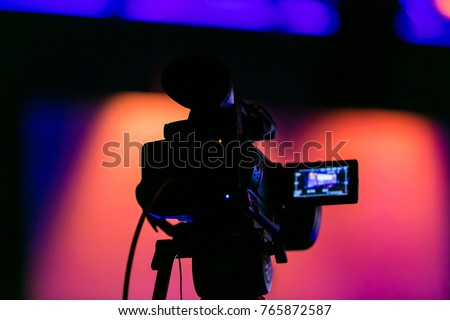 Silhouette of a video camera capturing an event on stage. Live streaming tv. Breaking news. News event. Story. Reporter. Live Broadcast