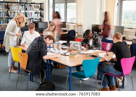 Busy College Library With Teacher Helping Students At Table