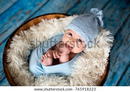 Little baby boy with knitted hat in a basket, happily smiling and looking at camera, isolated studio shot Royalty-Free Stock Photo #765918223