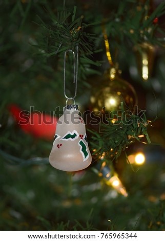 Holiday bell hanging on a Christmas tree with yellow tree lights in the background, vertical format.