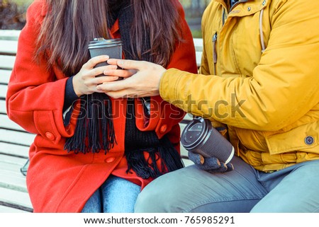 couple talking and flirting while drink coffe outside in city park on the bench