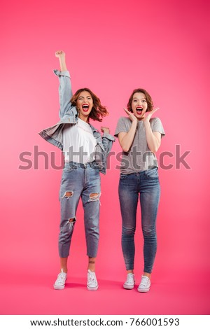 Picture of excited two ladies friends standing isolated over pink background. Looking camera.