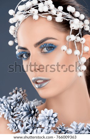 attractive model with hair accessory, christmas pine cones, winter makeup and glitter, isolated on grey