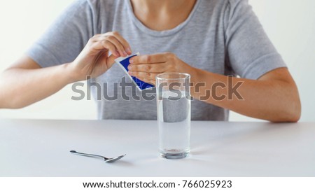 healthcare, medicine and people concept - close up of woman with glass of water and spoon opening pack of medication