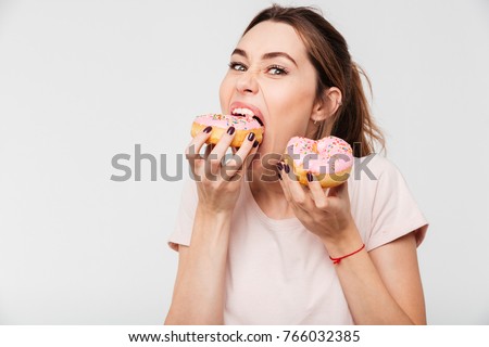 Close up portrait of a hungry greedy girl eating donuts isolated over white background Royalty-Free Stock Photo #766032385