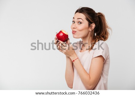 Close up portrait of a lovely pretty girl biting an apple isolated over white background Royalty-Free Stock Photo #766032436