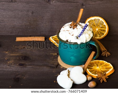 Christmas coffee cup with whipped cream, cinnamon, cocoa powder, anise, dried orange ang gingerbread cookies on wooden table. Dark retro style with copy space. 