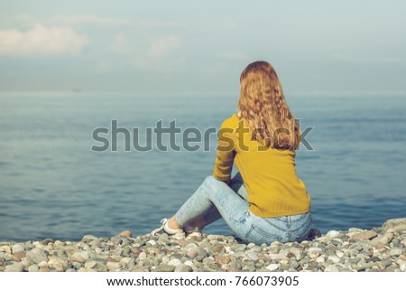 beautiful blonde girl is sitting on the beach and looking at the horizon.