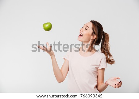 Portrait of a smiling happy girl throwing apple in the air isolated over white background Royalty-Free Stock Photo #766093345