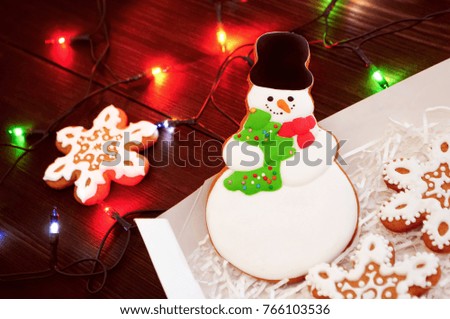 Christmas gingerbread snowman and snowflakes in box on a dark table with light garlands. Concept of new year gift. Picture for a confectionery catalog. Invitation or greeting card with copy space.