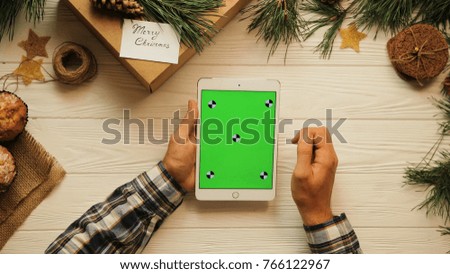 View from above. Male hands tapping, scrolling and zooming on tablet divice vertically. The white desk with Christmas stuff. Green screen, chroma key. Tracking motion.