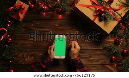 Top view. Woman tapping, scrolling and zooming on the mobile phone vertically. The decorated wooden desk with garlands. Christmas stuff. Green screen, chroma key.