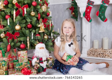 Christmas or New year celebration. Young beautiful girl in the hands holding christmas gift sitting near Christmas tree. A fireplace with christmas stocking on background