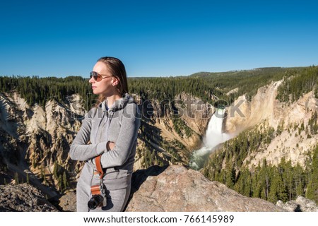 Woman tourist with camera overlooking Lower Falls waterfall in the Grand Canyon of Yellowstone National Park, Wyoming, USA
