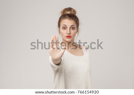 Blone young adult woman showing stop or ban sign. Studio shot, gray background