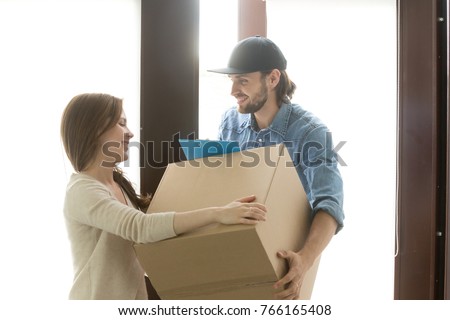 Delivery service concept, woman receiving cardboard box from man at home standing in hallway door, customer taking package accepting postal parcel, courier delivering container to recipient Royalty-Free Stock Photo #766165408
