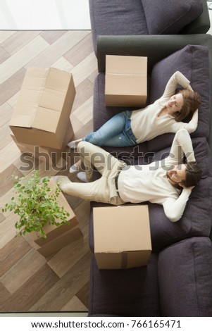Couple man and woman sitting on sofa in living room hands behind head, happy young homeowners relaxing on couch after packing boxes, easy relocation with moving delivery service concept, top view Royalty-Free Stock Photo #766165471