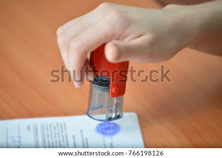 Female hand hold rubber stamps over documents and papers at office table, closeup detail shoot.