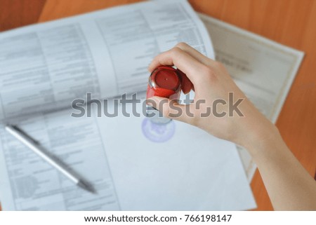 Female hand hold rubber stamps over documents and papers at office table, closeup detail shoot.
