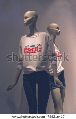 Window display with five mannequins wearing t-shirts with text sale