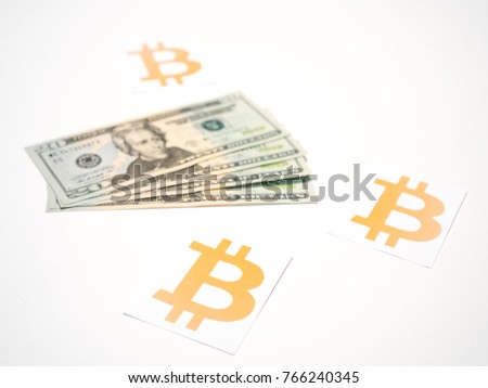 Close up photograph of a fanned out pile of US 20 dollar bills next to gold bitcoin crypto currency symbol on white background.
