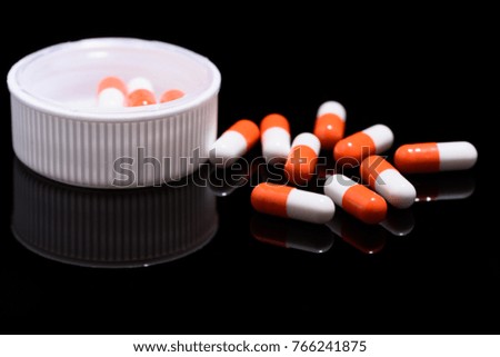 Medical and health care concept: capsules scattered on reflective black background.
