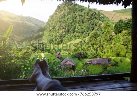 Man legs of traveler sitting on wooden pavilion above village and rice field in the countryside
