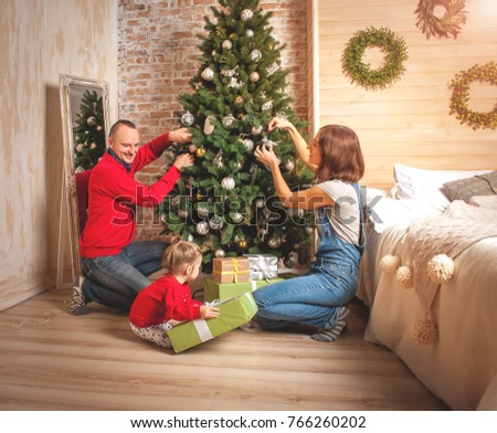 Dad, mom and daughter decorate a Christmas tree. Happy loving family opening gifts. Christmas tree with presents under it. decorated living room. 