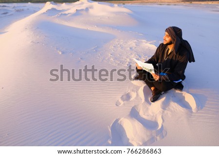 Educated male Muslim builder or designer works with drawings and inspects terrain for future construction, sitting in large desert at sunset on summer evening against backdrop of beautiful sky