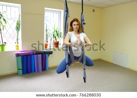 Beautiful girl of American appearance performs acrobatic elements in air, child concentrates and calmly holds on acrobatic ropes. Room nice warm lighting, walls delicate yellow and large windows, on