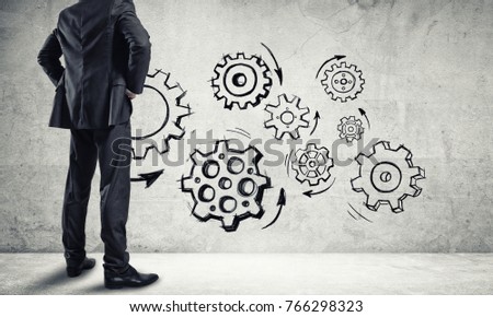 Back view of businessman looking at wall with drawn gear mechanism