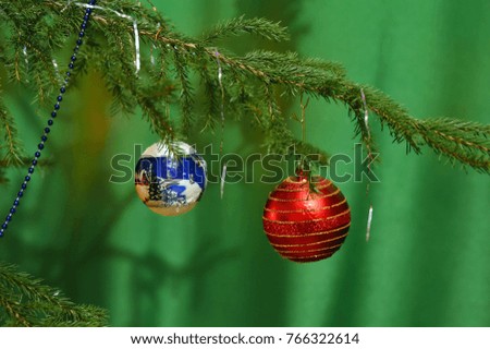 The branch of the Christmas tree is decorated with two balls: red and blue with a pattern.