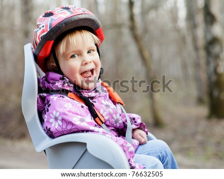 Happy little girl wearing helmet sitting in bycicle child seat
