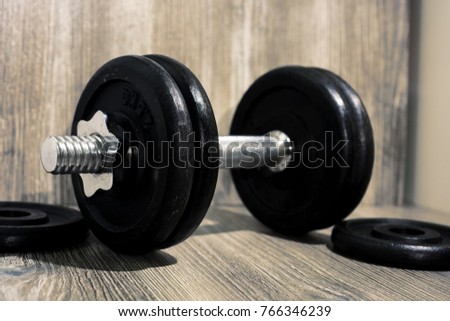Black dumbbell on wooden background. Sport abstraction.