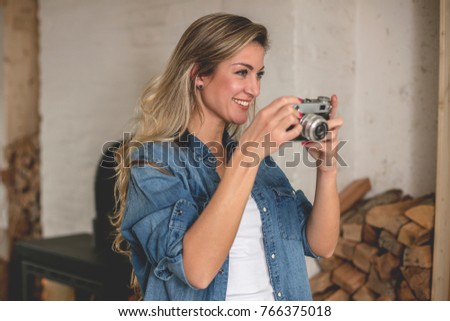 Indoor smiling lifestyle portrait of pretty young woman with camera