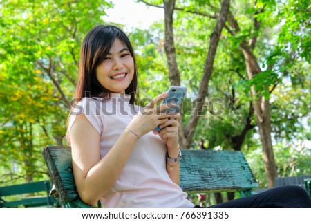 Smiling women relaxing use cellphone in public park siting on bench