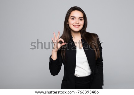 Close up portrait of a cheerful young business woman showing okay gesture isolated over gray