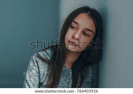 Photo of Expression of lonely female teenager at home. Portrait of a sad teenage girl looking thoughtful about troubles. Pensive teen. Depression, teen depression, pain, suffering.