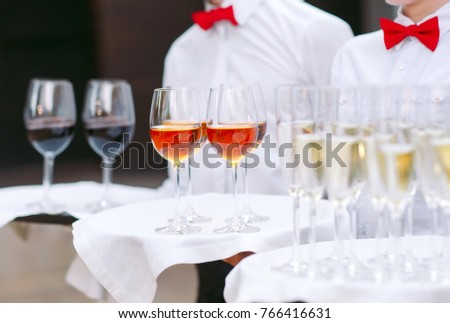 The waiters greet guests with alcoholic drinks. Champagne, red wine, white wine on trays.