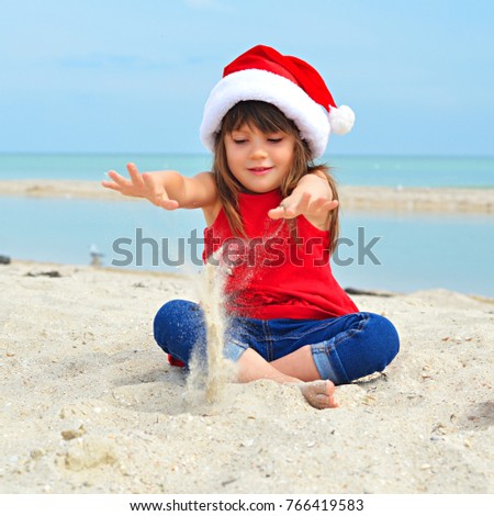 Cute little girl celebrating Christmas and New Year holidays on the beach, playing with sand