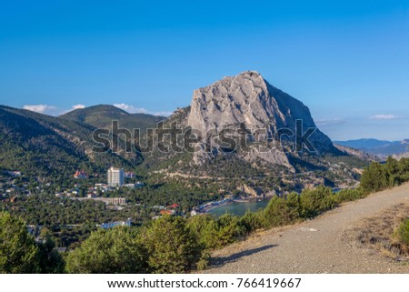 View from mountain stony path on thicket, marine town near Black sea bay and mountains above town in distance under clean blue sky in Crimea
