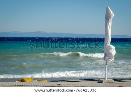 stormy sea with many waves on empty beach with white umbrella on sunny windy day 
